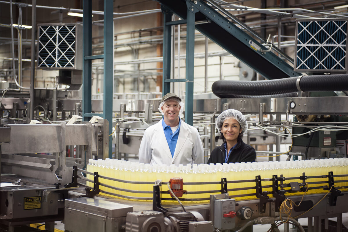 Two workers by a conveyor belt of lemon flavored water in a bottling plant.